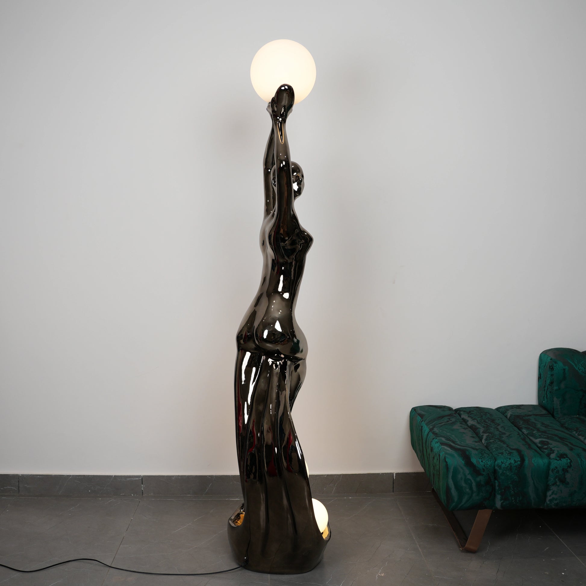 Black floor lamp shaped like a woman with a round light bulb on a gray floor.