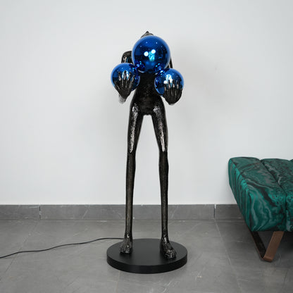 Black abstract sculpture with blue spherical objects on a gray floor.