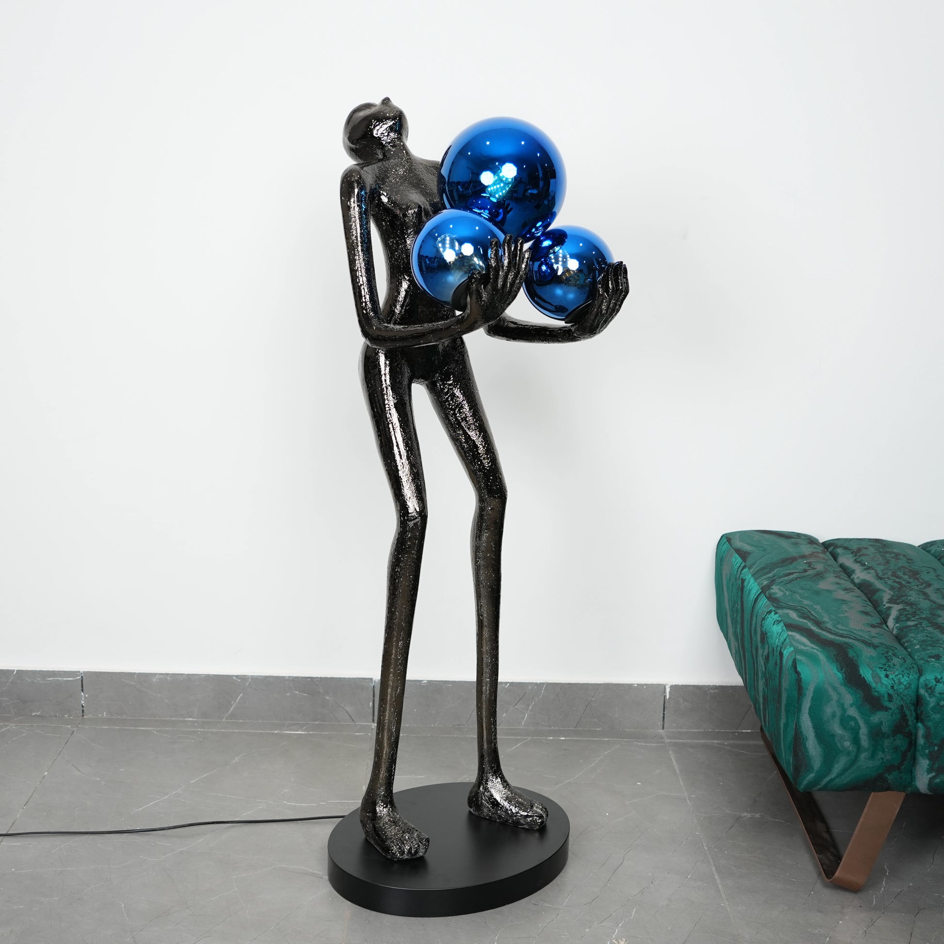 Abstract sculpture of a figure holding blue spheres in a room with a green couch.