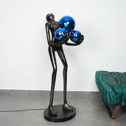 Abstract sculpture of a figure holding blue spheres in a room with a green couch.