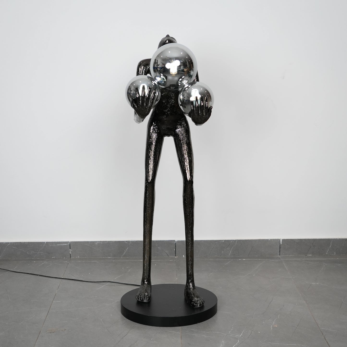 Black abstract sculpture on a gray floor with a white wall background