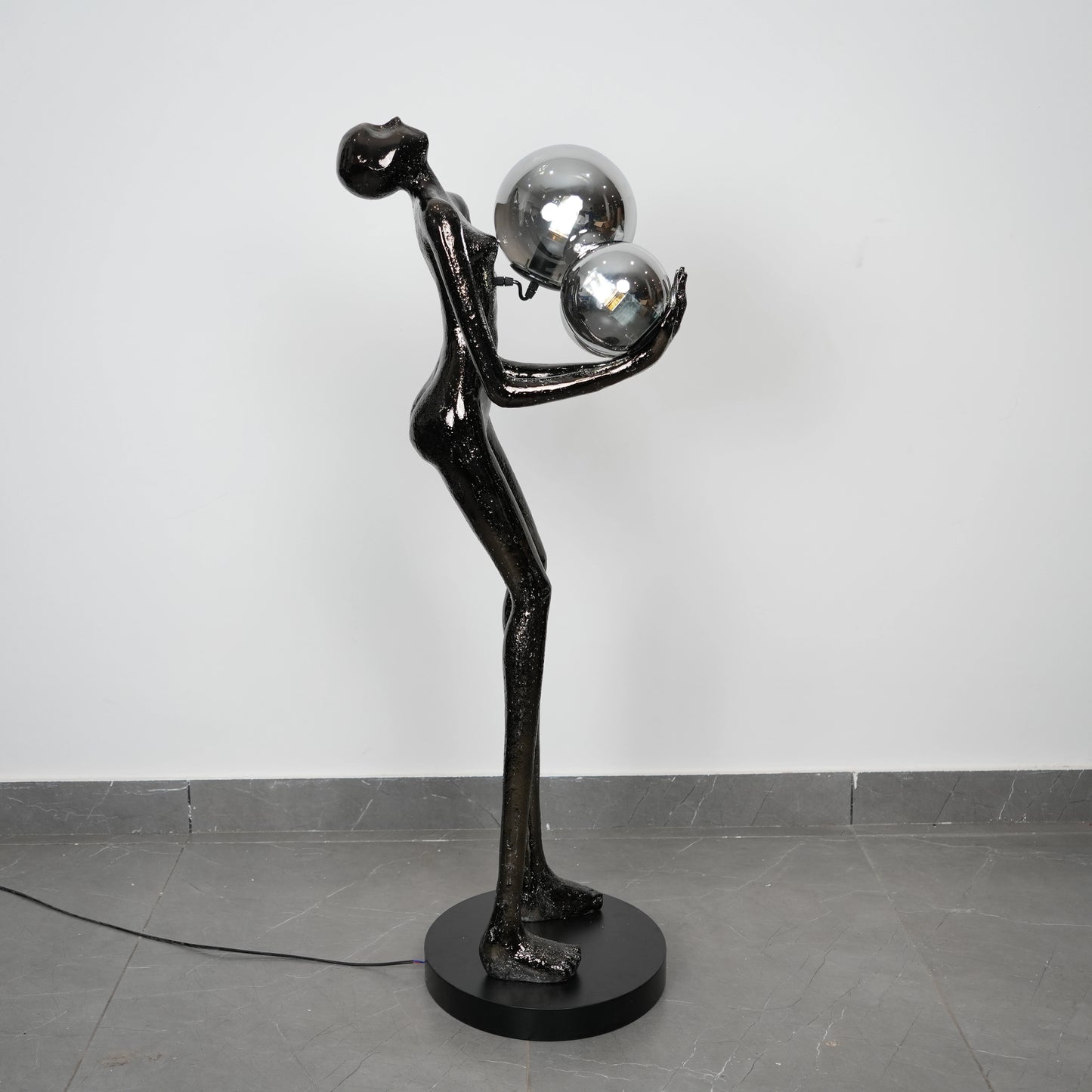 Black abstract sculpture with spherical elements on a gray floor against a white wall
