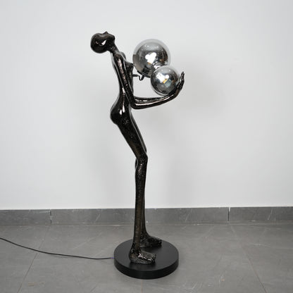 Black abstract sculpture with spherical elements on a gray floor against a white wall