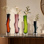 Set of four artistic sculptural glass vases in dark brown, blush pink, lime green, and charcoal, featuring glossy transparent glass bases, elegant curved silhouettes, and unique organic branch-like detailing, displayed together on a clean white studio background.