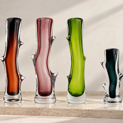 Set of four artistic sculptural glass vases in dark brown, blush pink, lime green, and charcoal, featuring glossy transparent glass bases, elegant curved silhouettes, and unique organic branch-like detailing, displayed together on a clean white studio background.