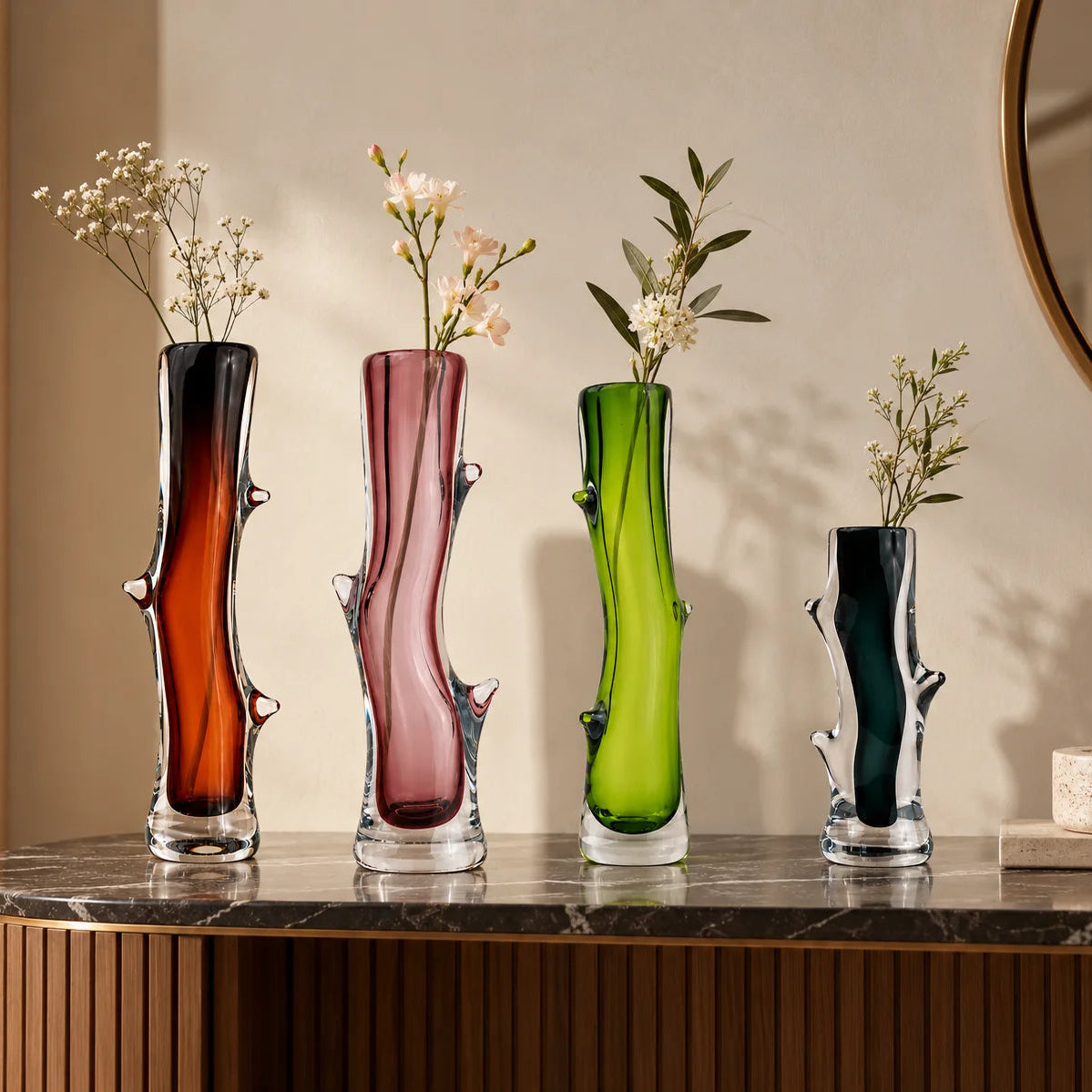 Set of four artistic sculptural glass vases in dark brown, blush pink, lime green, and charcoal, featuring glossy transparent glass bases, elegant curved silhouettes, and unique organic branch-like detailing, displayed together on a clean white studio background.