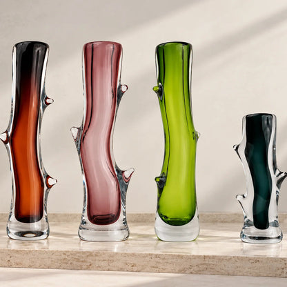 Set of four artistic sculptural glass vases in dark brown, blush pink, lime green, and charcoal, featuring glossy transparent glass bases, elegant curved silhouettes, and unique organic branch-like detailing, displayed together on a clean white studio background.