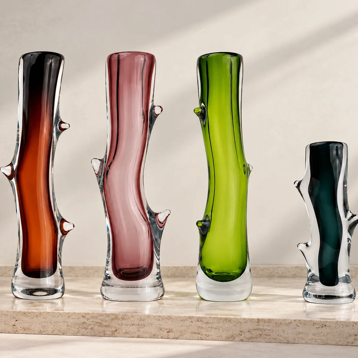 Set of four decorative glass vases in brown, pink, lime green, and charcoal, featuring artistic curves, transparent glass bases, and unique sculptural detailing.