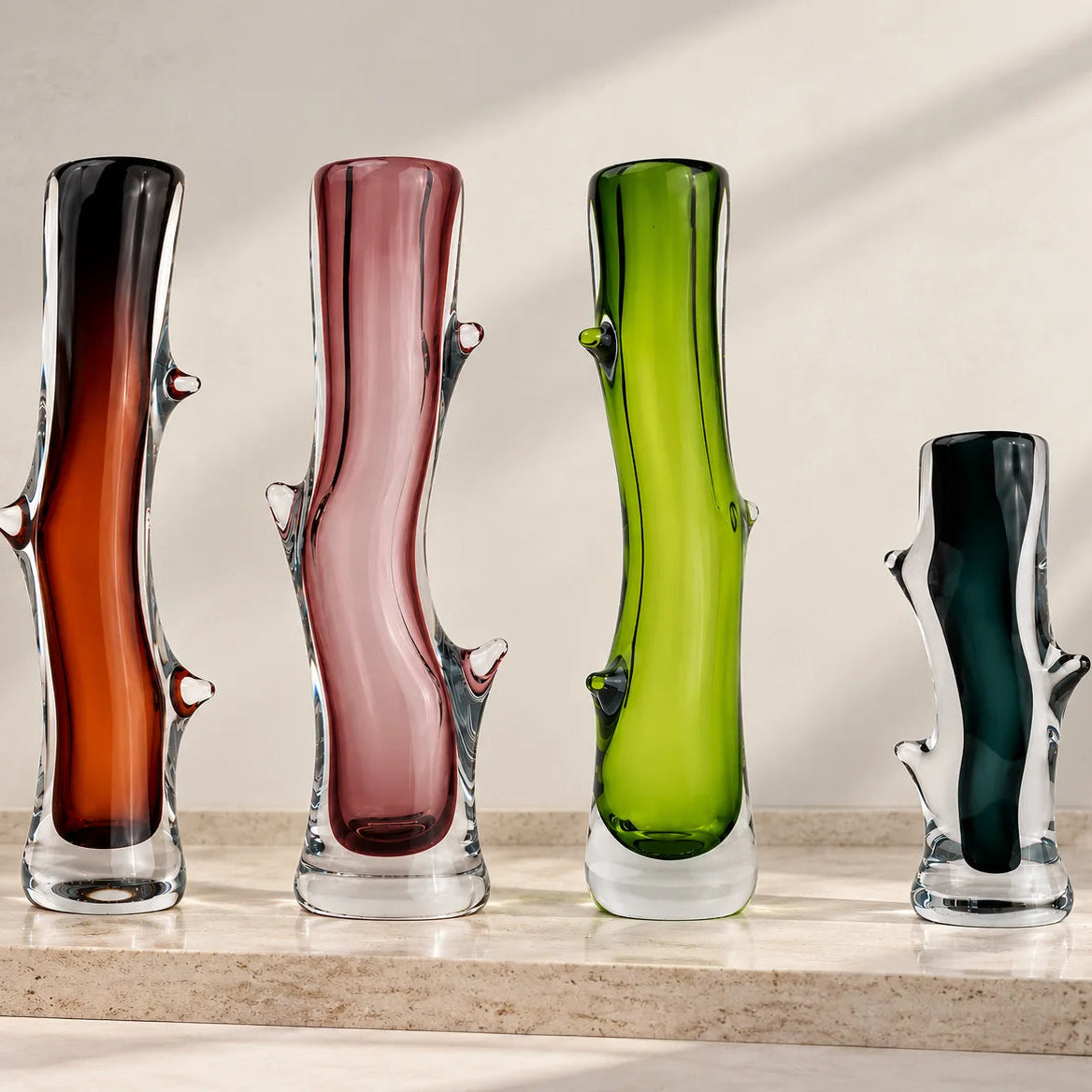 Set of four decorative glass vases in brown, pink, lime green, and charcoal, featuring artistic curves, transparent glass bases, and unique sculptural detailing.