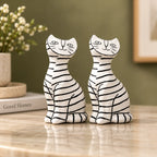 Two resin cat figurines with black stripes on a white glaze, displayed side-by-side on a polished marble countertop in a styled home setting.