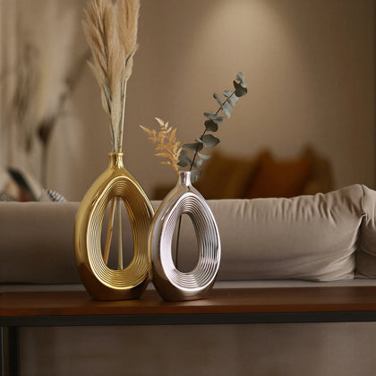 Luxury duo set of ceramic vases featuring contemporary hollow oval silhouettes in gold and silver finishes, ideal for fresh flowers, dried botanicals, console tables and modern designer interiors.