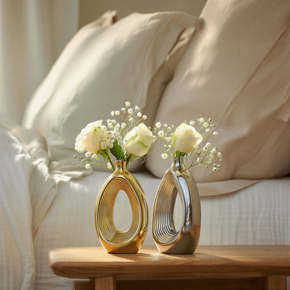 Luxury duo set of ceramic vases featuring contemporary hollow oval silhouettes in gold and silver finishes, ideal for fresh flowers, dried botanicals, console tables and modern designer interiors.