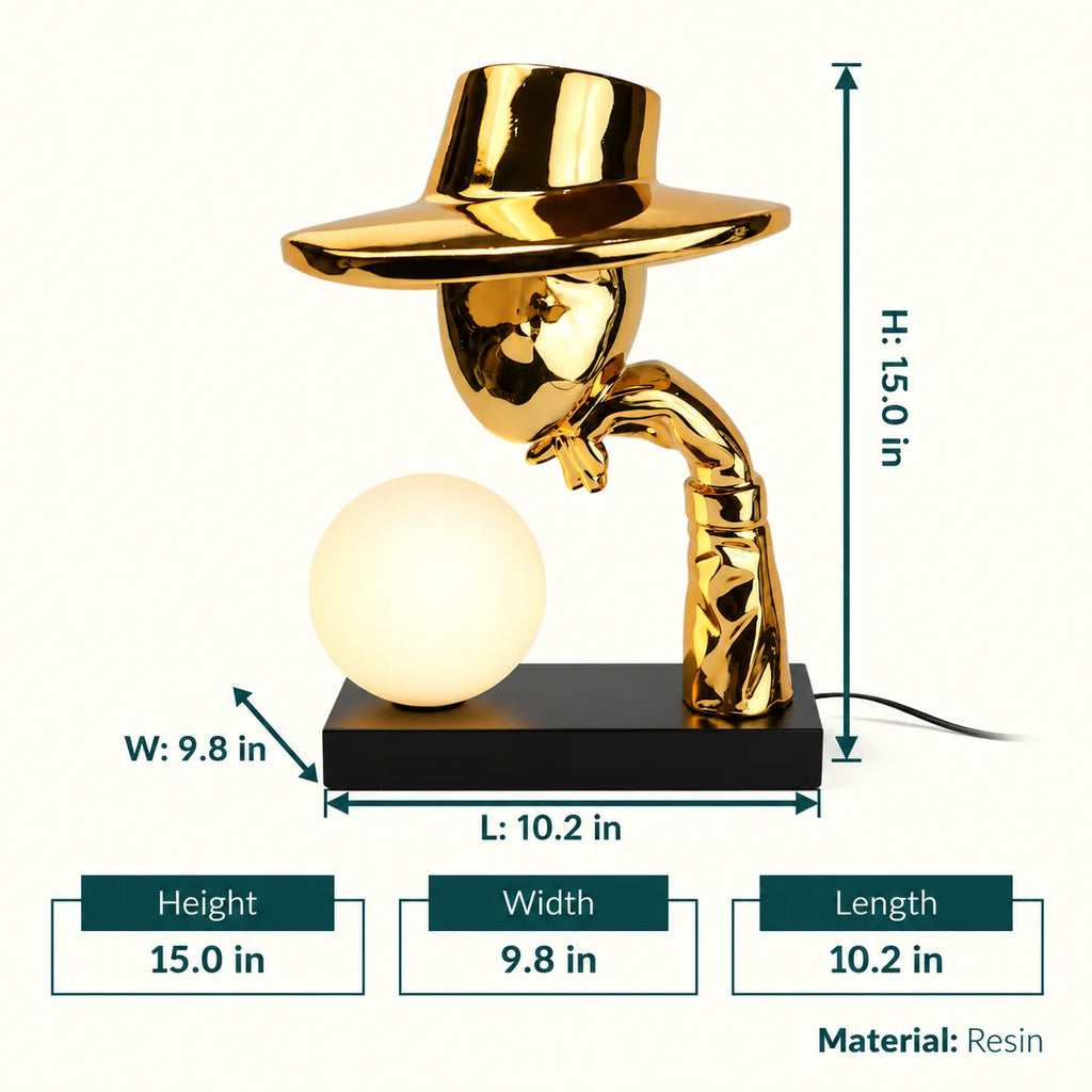 Gold electroplated table lamp featuring a sculptural curved human-like form with a wide hat-shaped top and a glowing spherical light on a rectangular base, designed with a smooth reflective metallic surface.