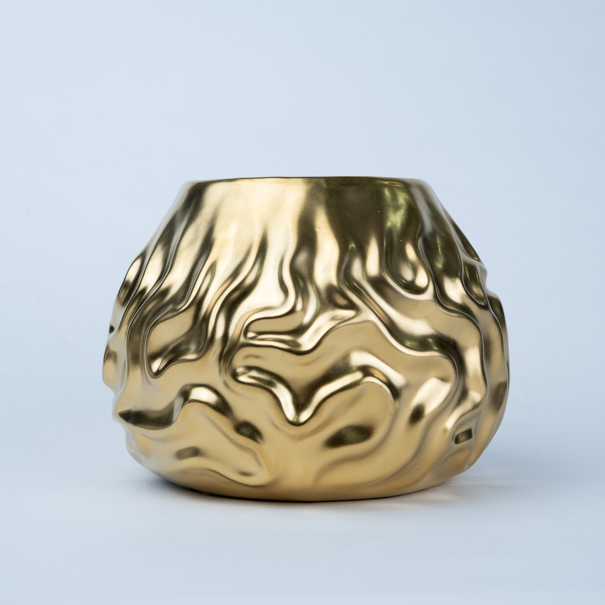 A metallic gold ceramic planter with a highly textured, fluid, wavy surface pattern, shown against a light blue-gray studio background.