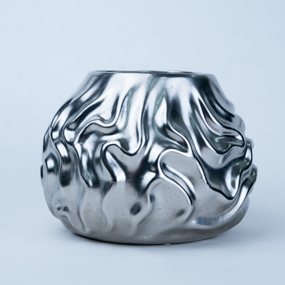 A metallic silver ceramic pot with a wavy, fluid, flame-like textured pattern, shown on a light gray background.