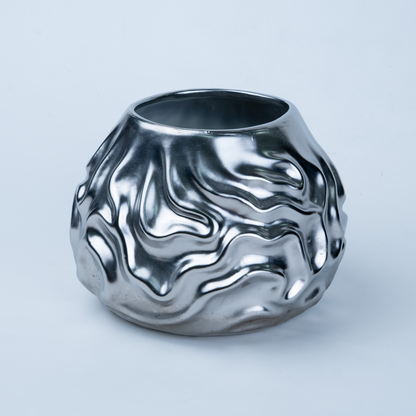 A metallic silver ceramic vase with a highly textured, fluid, wavy surface pattern, photographed on a clean light gray background.