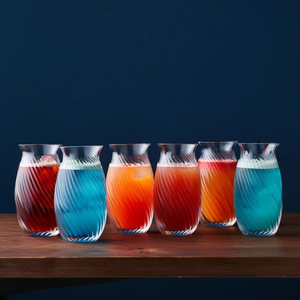 Six glass carafes filled with colorful liquids on a wooden surface against a dark blue background