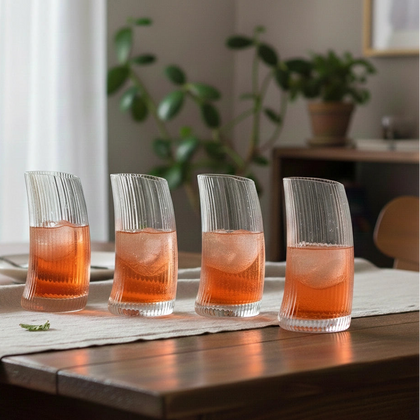Four glasses of orange cocktail with ice on a wooden table, blurred indoor background