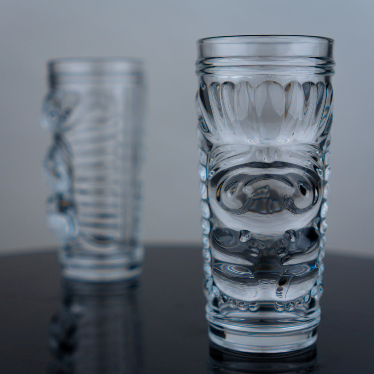Tiki glasses pair, embossed face, dark surface