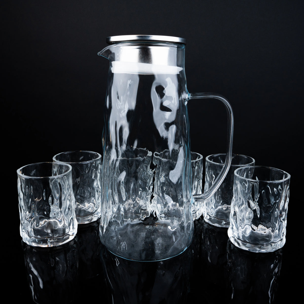 Clear glass pitcher and tumblers on a black background