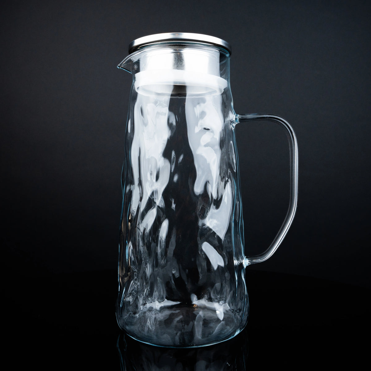 Clear glass pitcher with metal lid on a black background