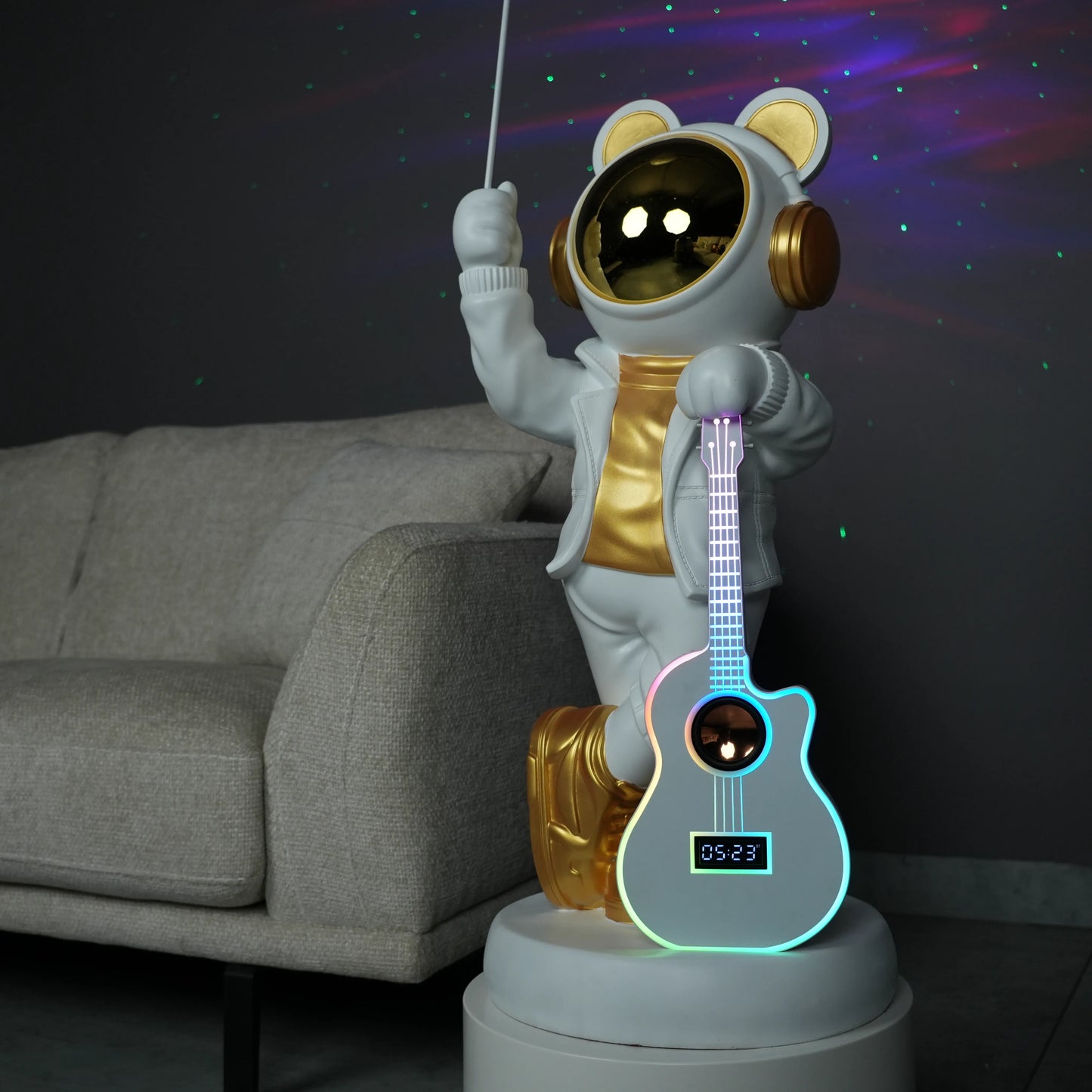White-and-gold astronaut statue holding a moon projector balloon with a guitar-shaped Bluetooth speaker, standing on a pedestal with galaxy projection in the background.
