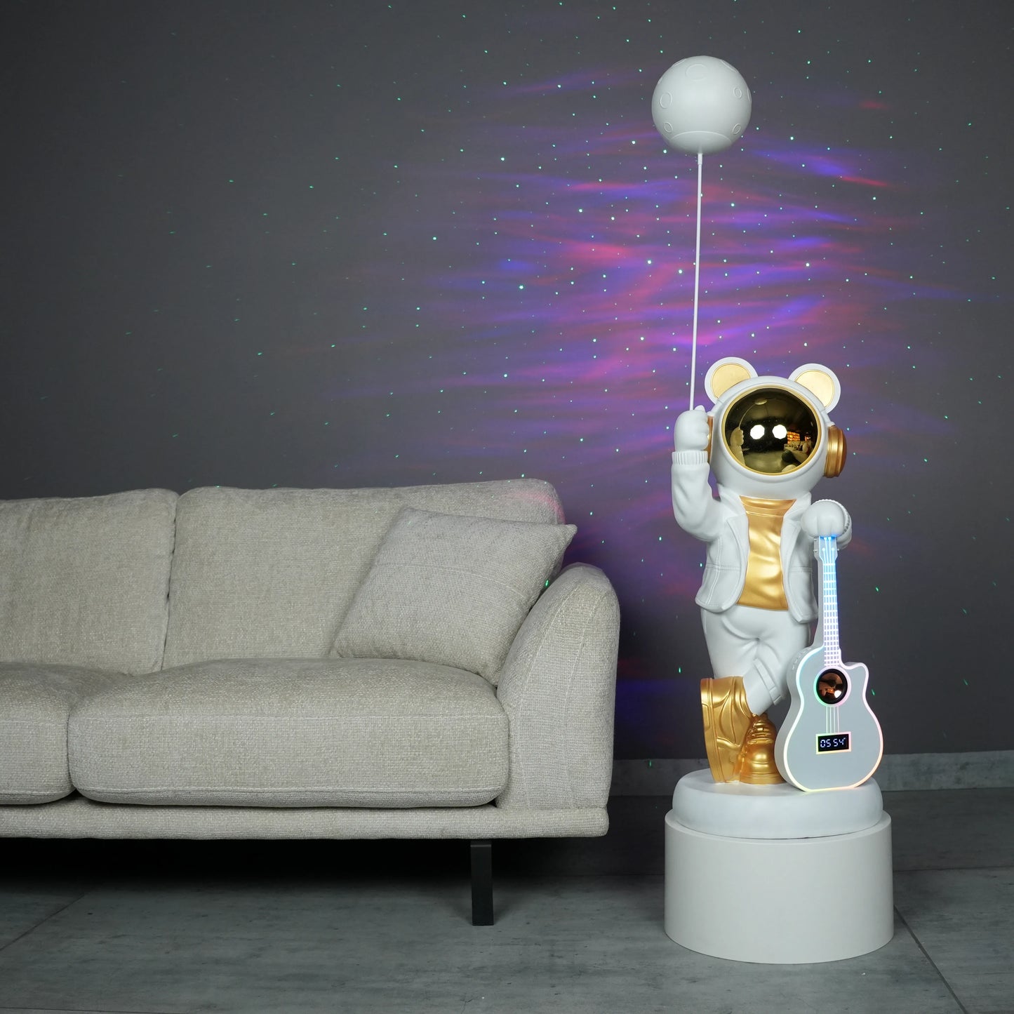 White-and-gold astronaut statue holding a moon projector balloon with a guitar-shaped Bluetooth speaker, standing on a pedestal with galaxy projection in the background.