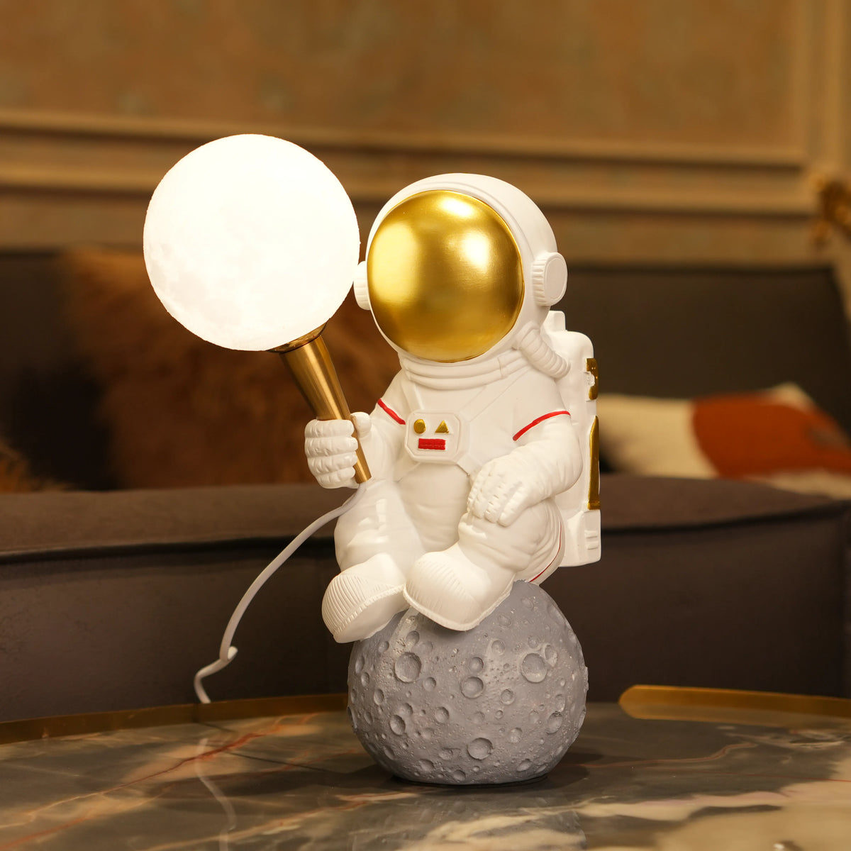 White astronaut figurine with a gold visor sitting on a textured grey moon while holding a glowing orb lamp, placed against a dark background.