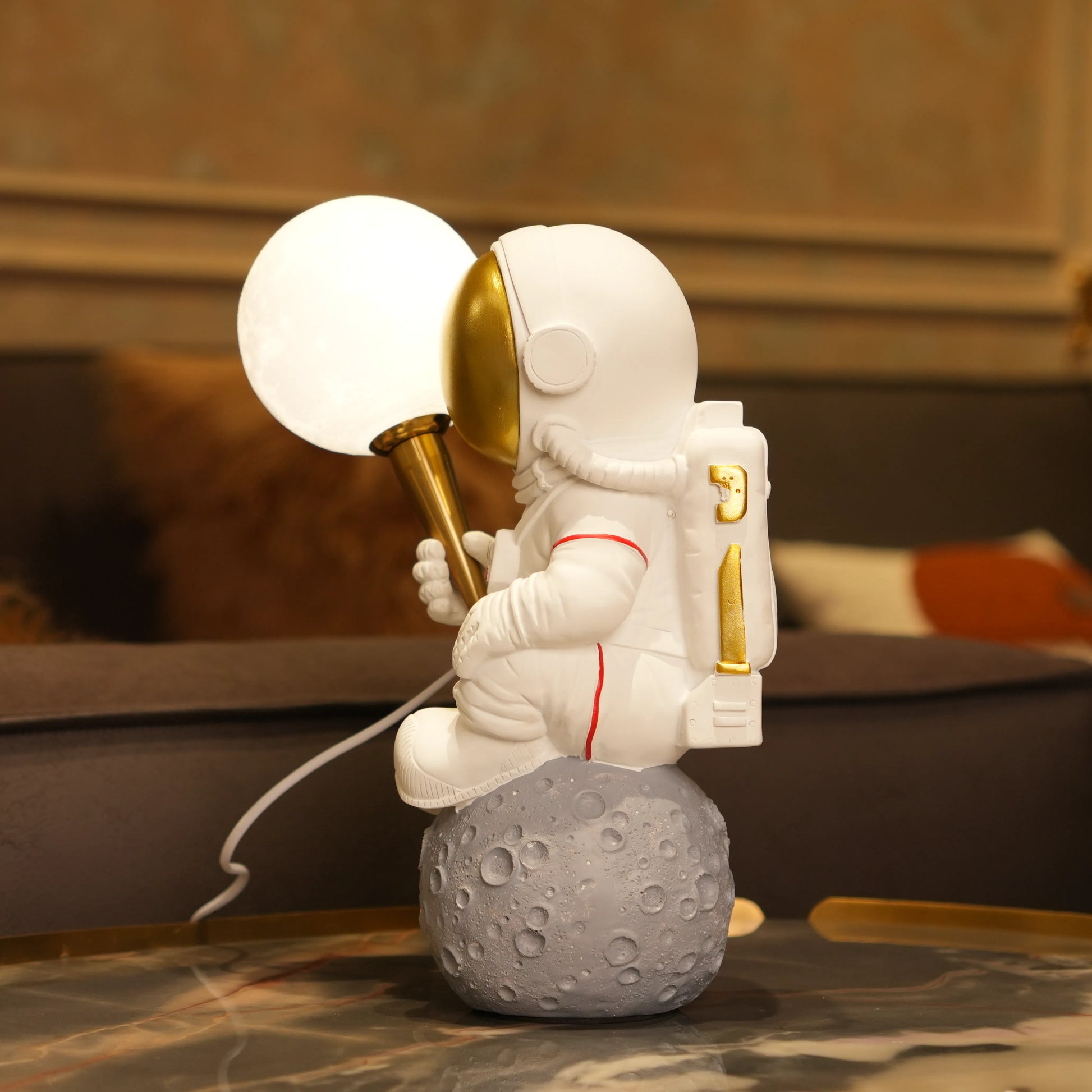 White astronaut figurine with a gold visor sitting on a textured grey moon while holding a glowing orb lamp, placed against a dark background.