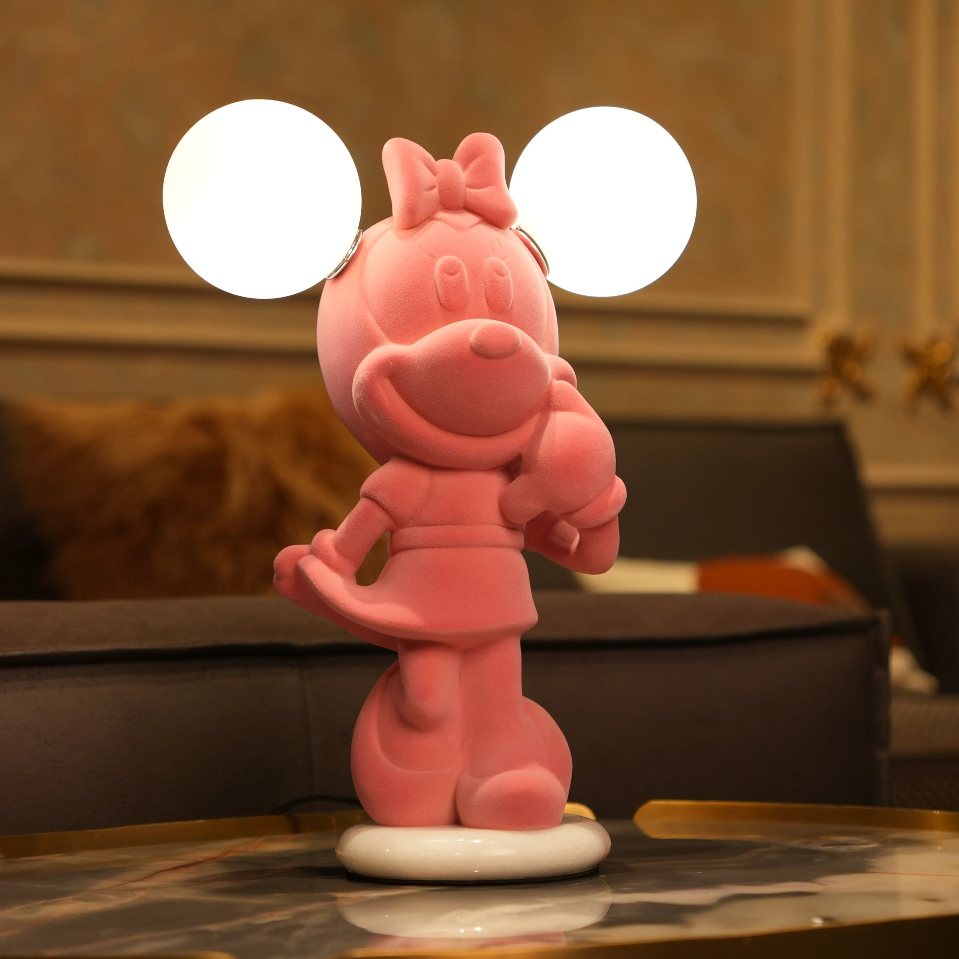 Standing pink flocked character lamp with two glowing ear-shaped bulbs on a white base.
