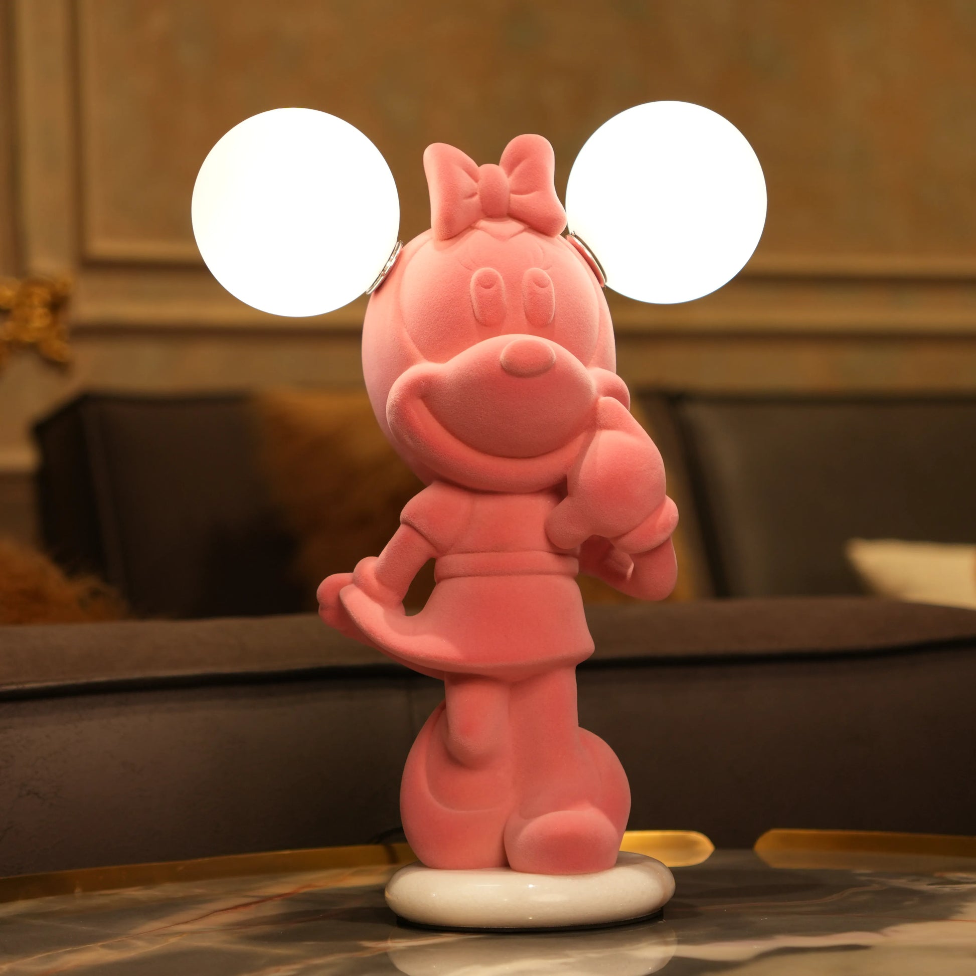 Standing pink flocked character lamp with two glowing ear-shaped bulbs on a white base.