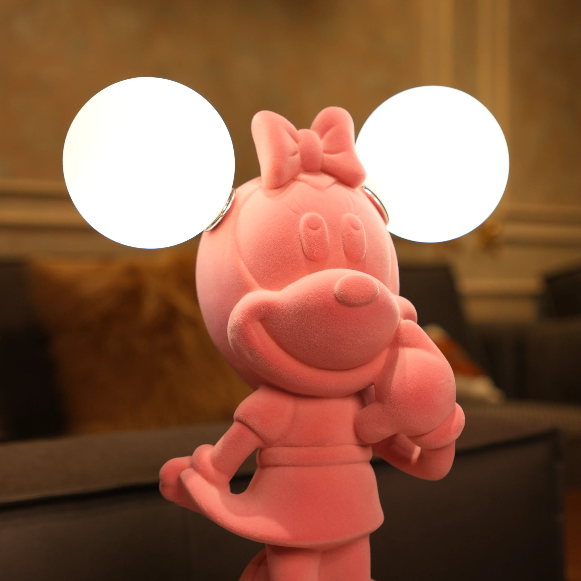 Standing pink flocked character lamp with two glowing ear-shaped bulbs on a white base.