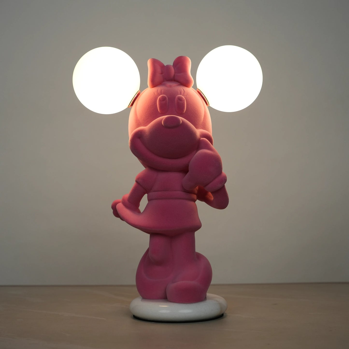 Standing pink flocked character lamp with two glowing ear-shaped bulbs on a white base.