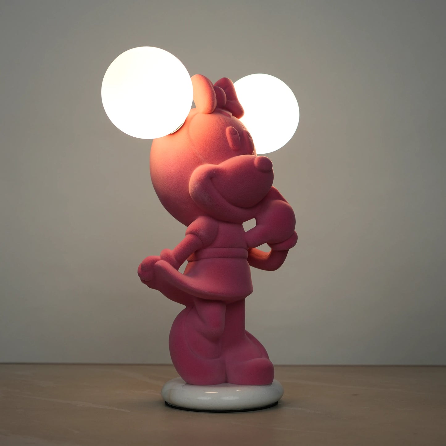 Standing pink flocked character lamp with two glowing ear-shaped bulbs on a white base.