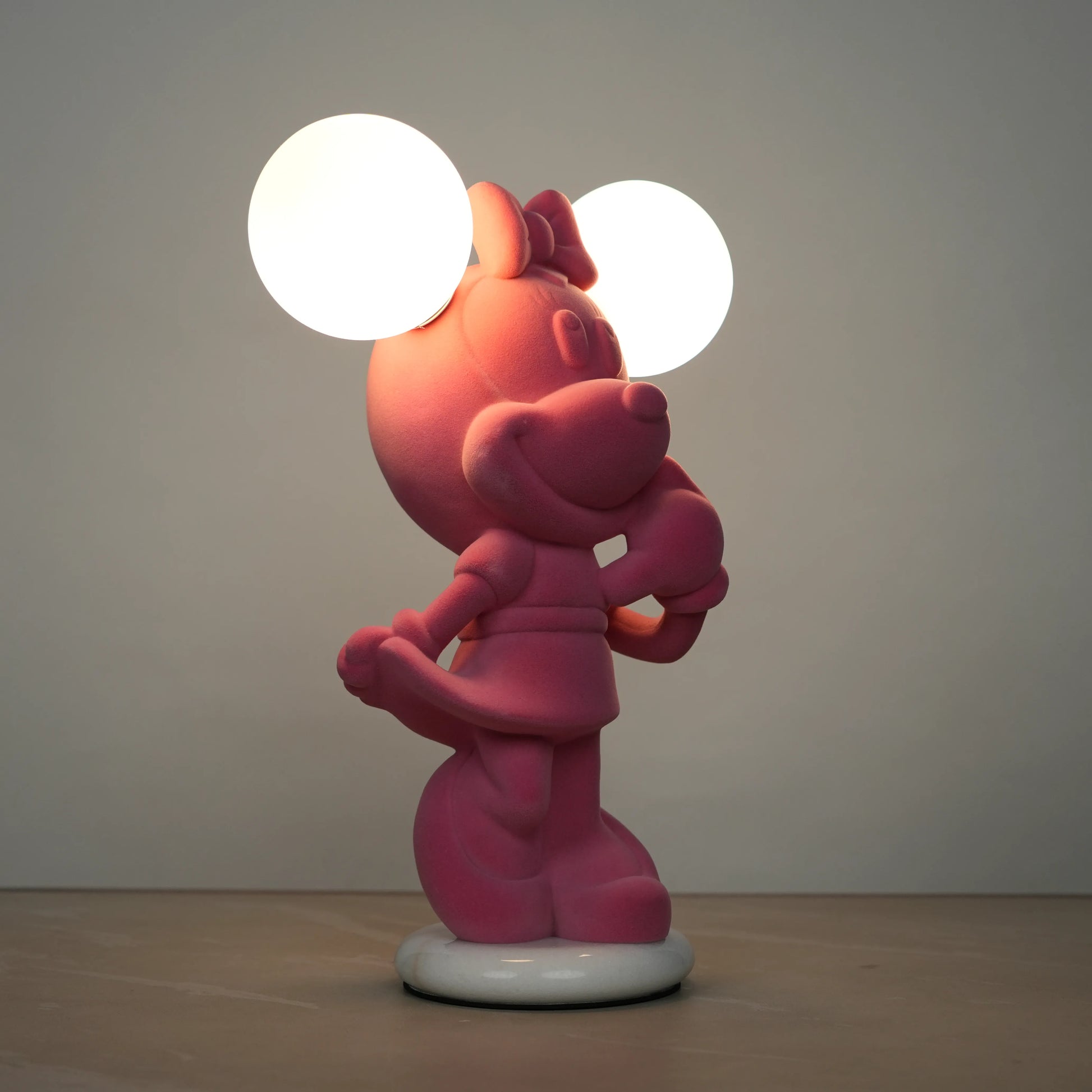 Standing pink flocked character lamp with two glowing ear-shaped bulbs on a white base.
