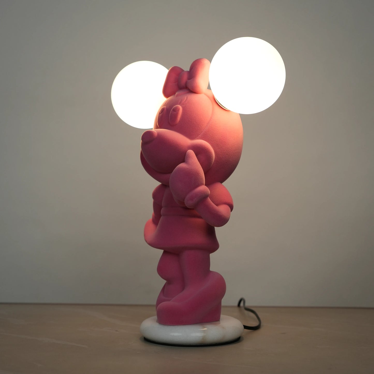 Standing pink flocked character lamp with two glowing ear-shaped bulbs on a white base.