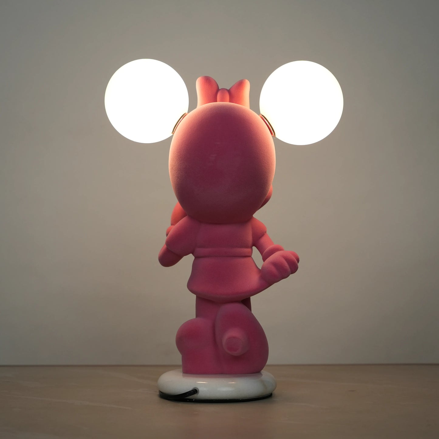 Standing pink flocked character lamp with two glowing ear-shaped bulbs on a white base.