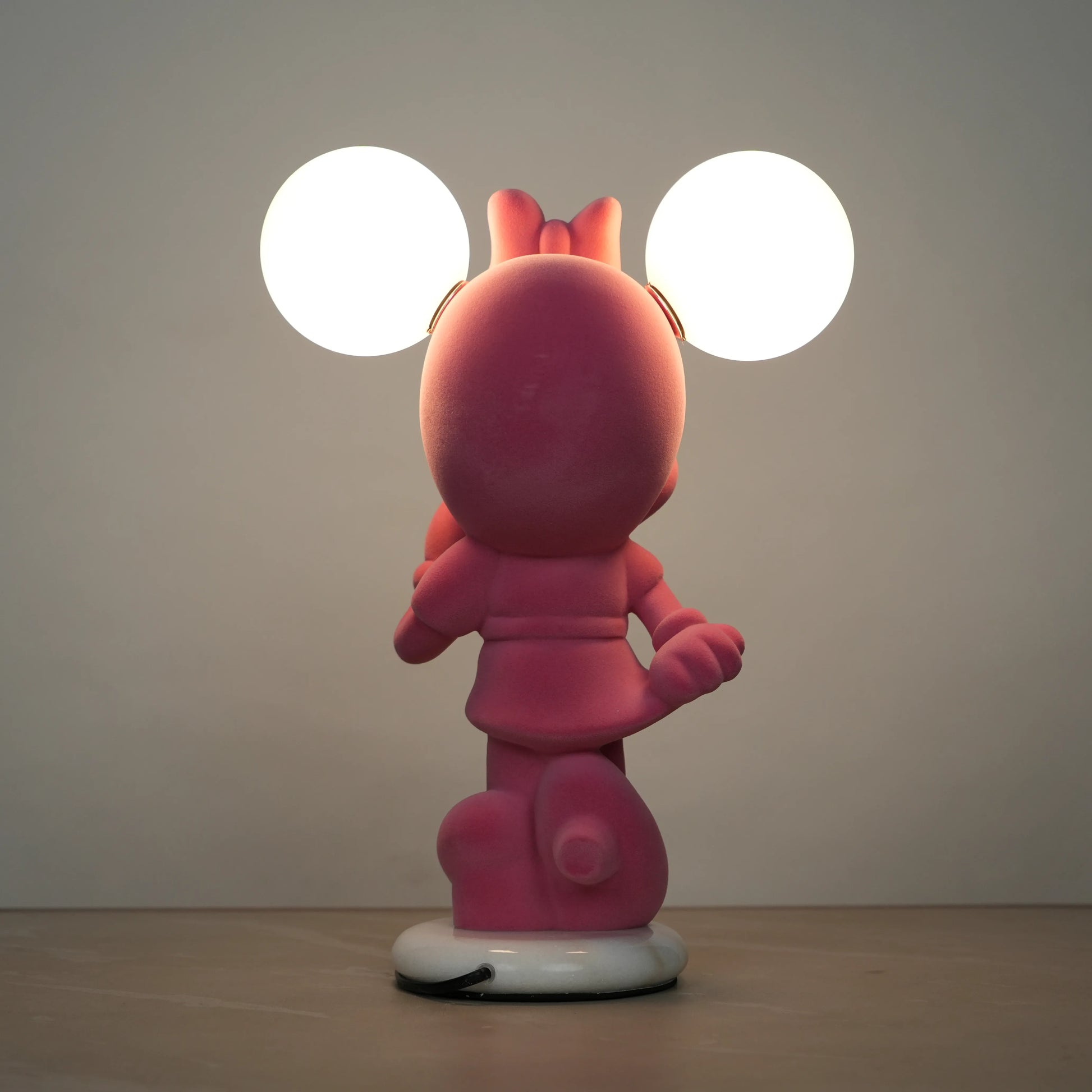 Standing pink flocked character lamp with two glowing ear-shaped bulbs on a white base.
