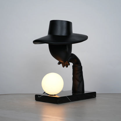Elegant Hat Lamp – Matte black faceless figurine with wide hat holding glowing orb on marble base – Ghar Art.