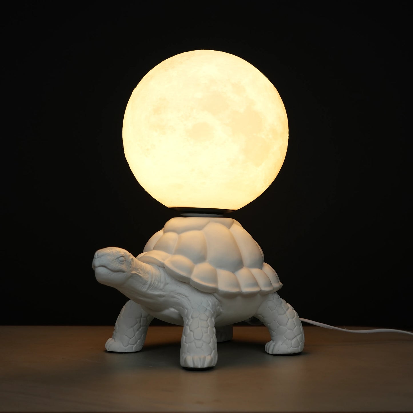 White tortoise sculpture lamp with a glowing moon orb placed on its shell.