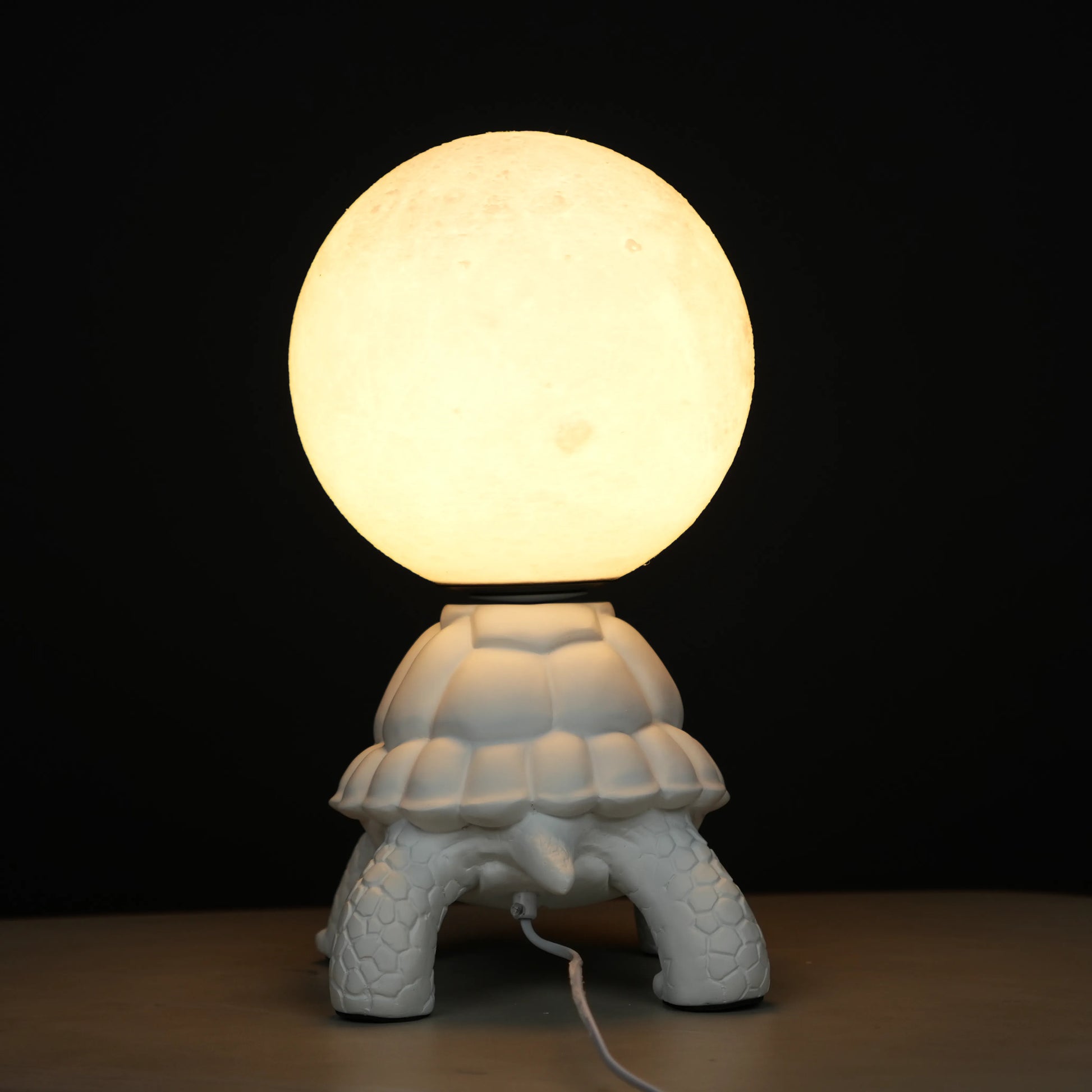 White tortoise sculpture lamp with a glowing moon orb placed on its shell.