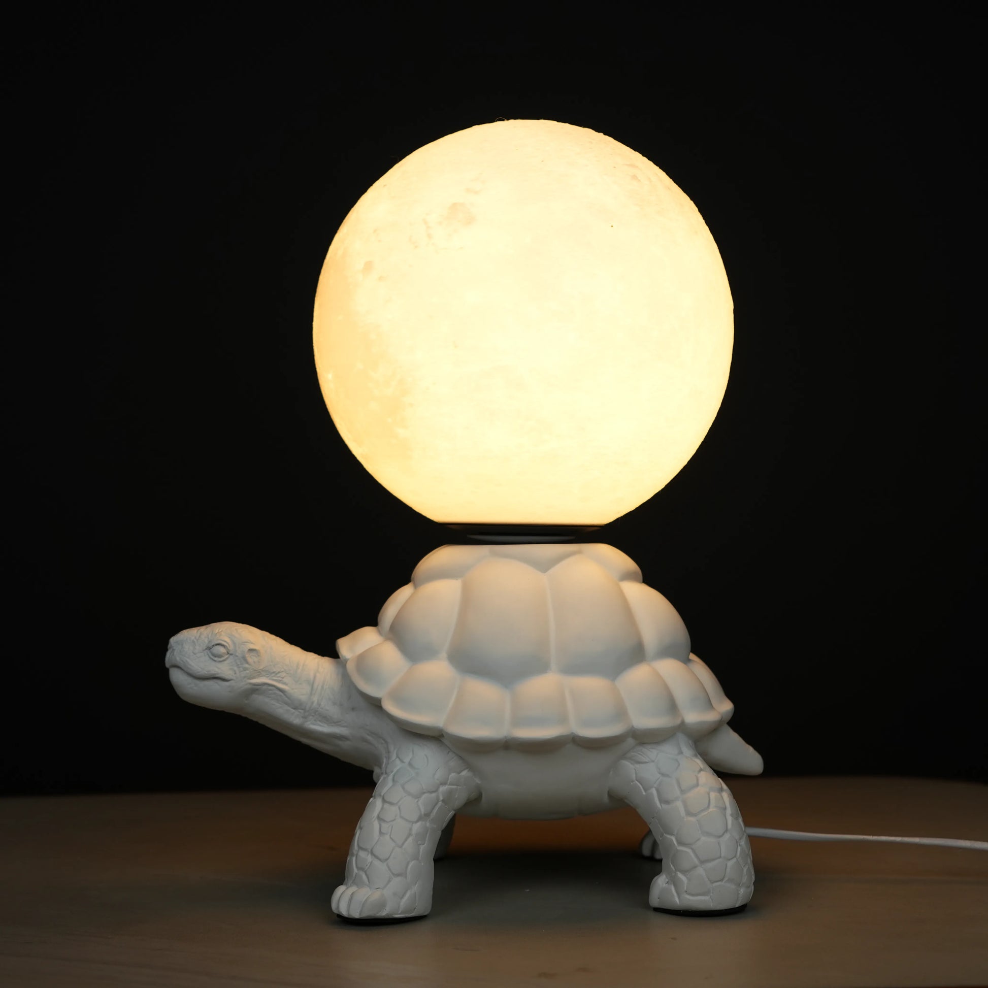 White tortoise sculpture lamp with a glowing moon orb placed on its shell.
