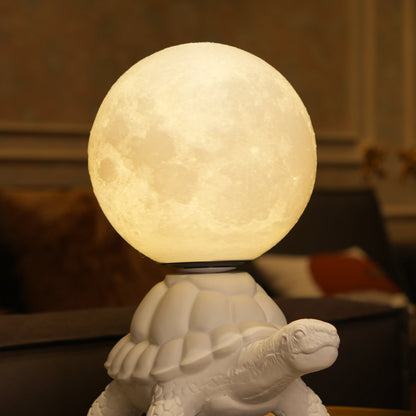 White tortoise sculpture lamp with a glowing moon orb placed on its shell.