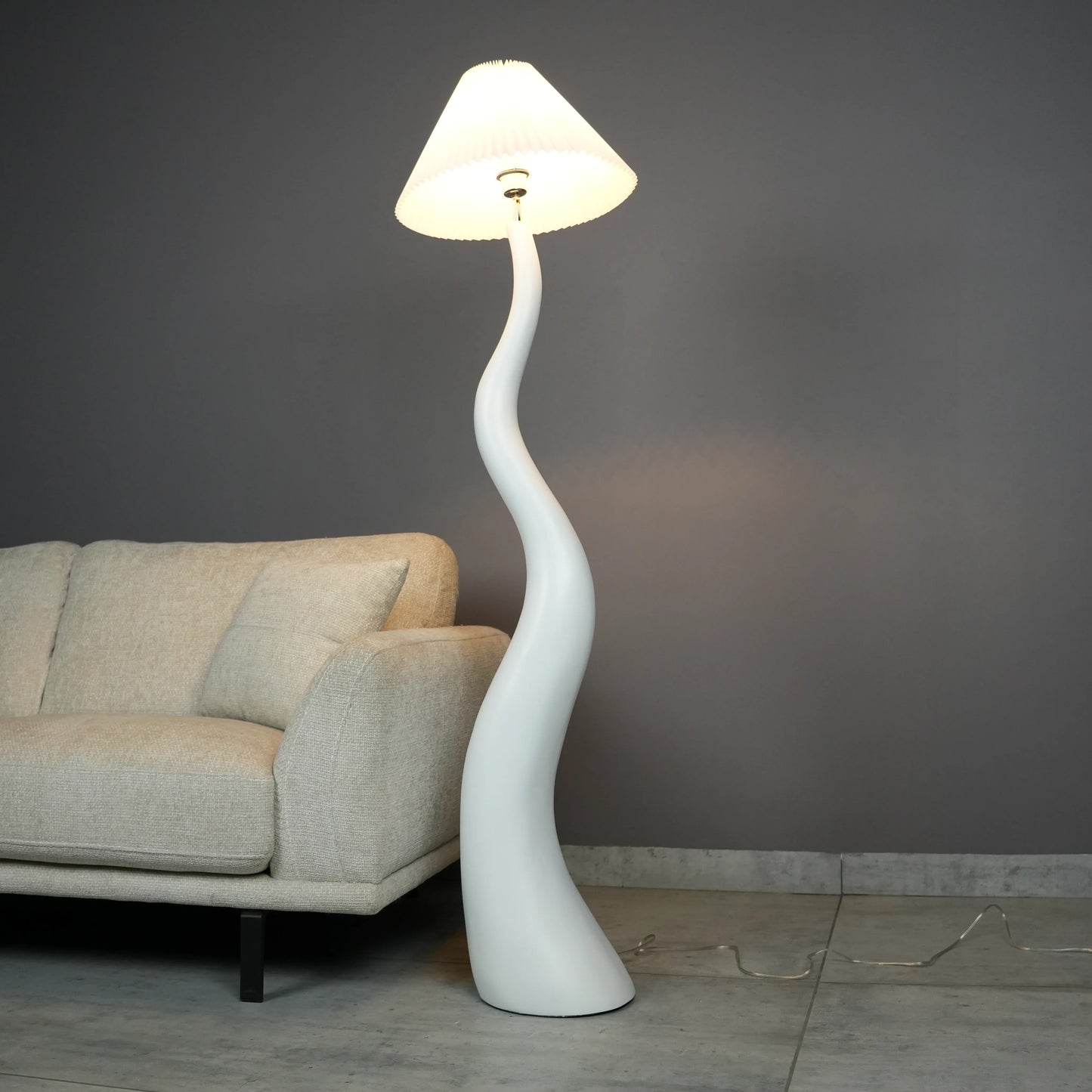 White wavy floor lamp with fabric shade placed beside sofa – modern sculptural lighting.”
