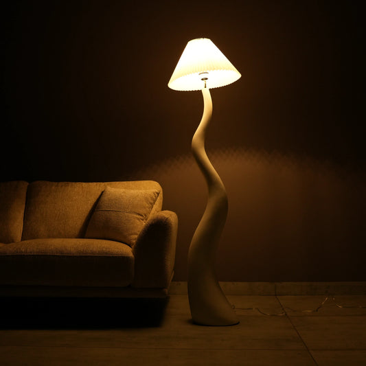 White wavy floor lamp with fabric shade placed beside sofa – modern sculptural lighting.”