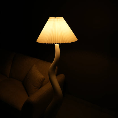 White wavy floor lamp with fabric shade placed beside sofa – modern sculptural lighting.”
