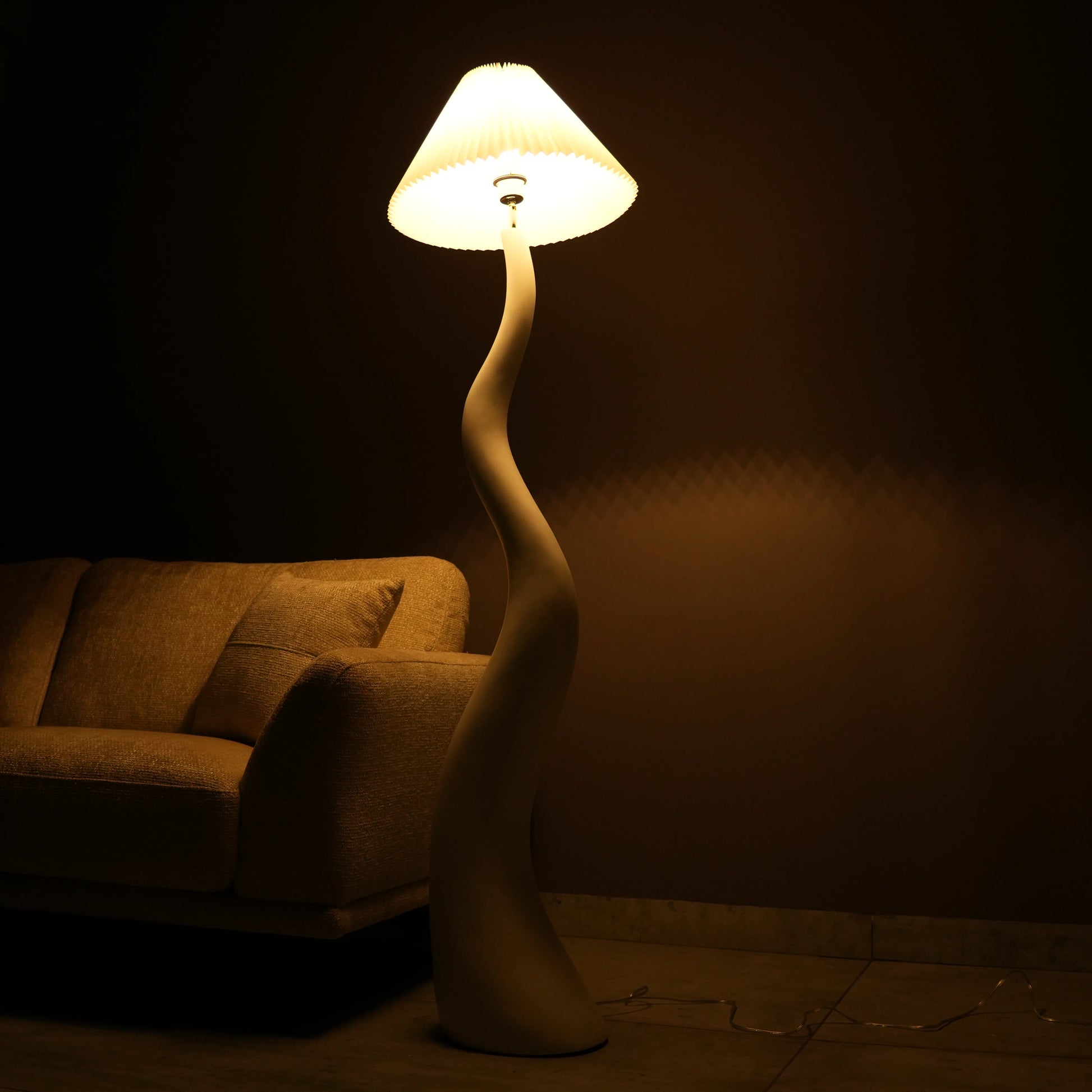White wavy floor lamp with fabric shade placed beside sofa – modern sculptural lighting.”