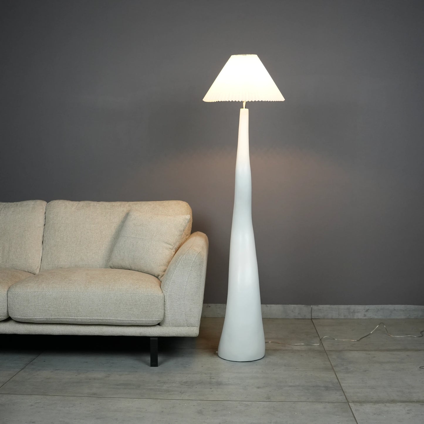 White wavy floor lamp with fabric shade placed beside sofa – modern sculptural lighting.”
