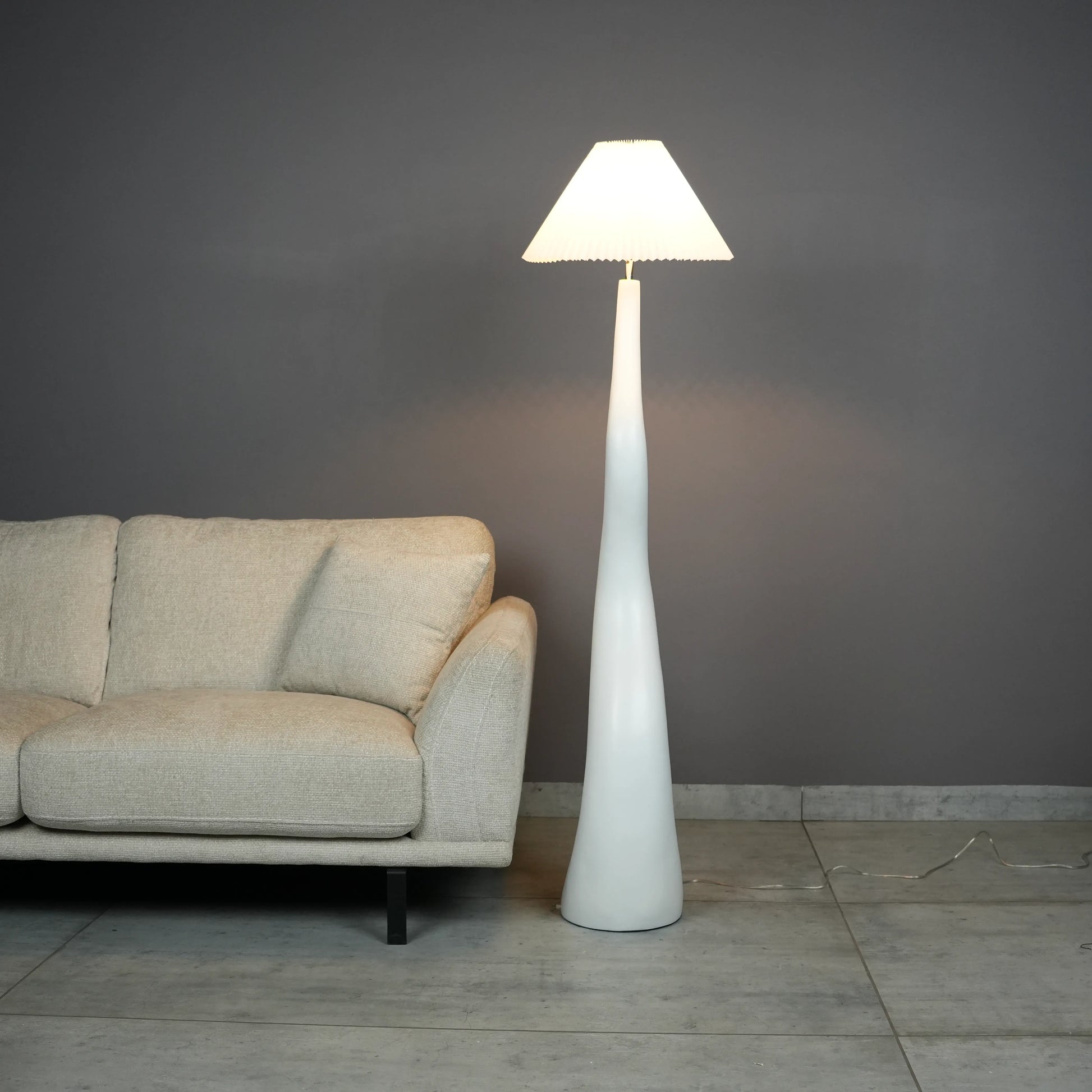 White wavy floor lamp with fabric shade placed beside sofa – modern sculptural lighting.”