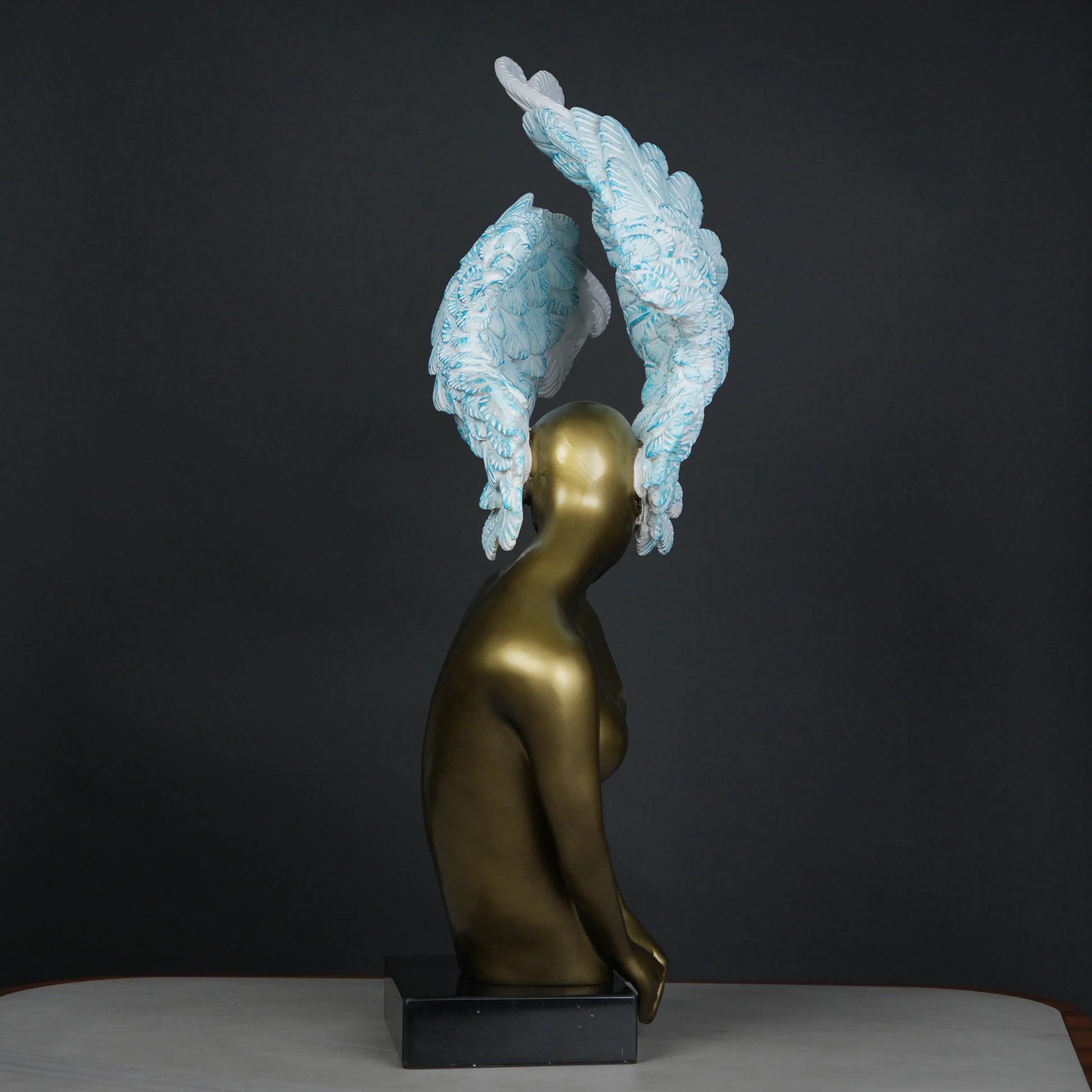 Gold-bodied woman sculpture with large white and blue feathered wings on a black base — luxury artistic décor piece.